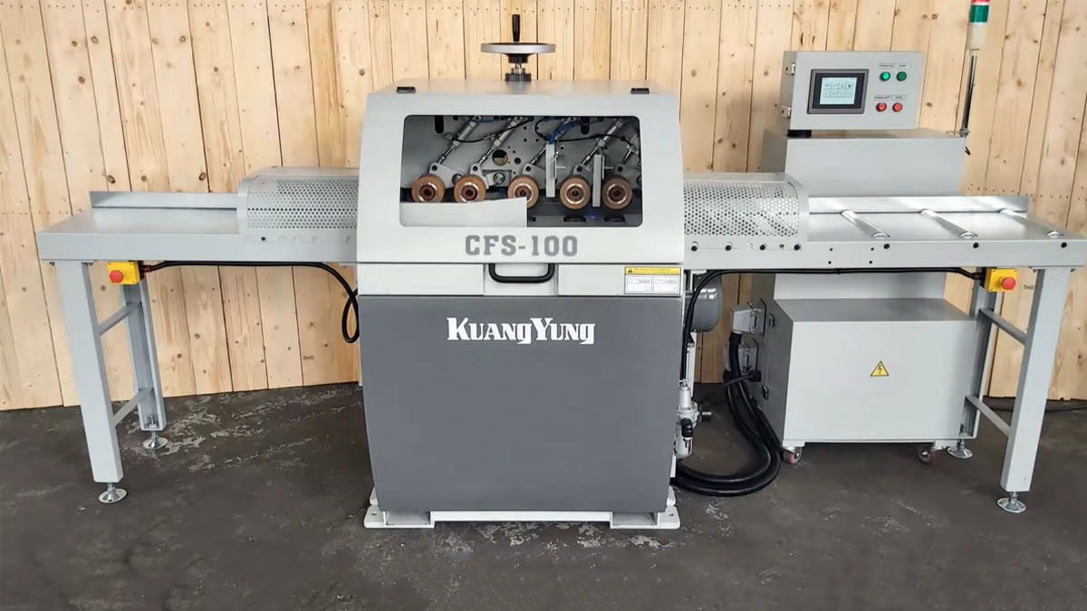 A conveyor system with multiple wooden planks being transported in a woodworking facility, featuring an industrial rip saw for processing the wood.