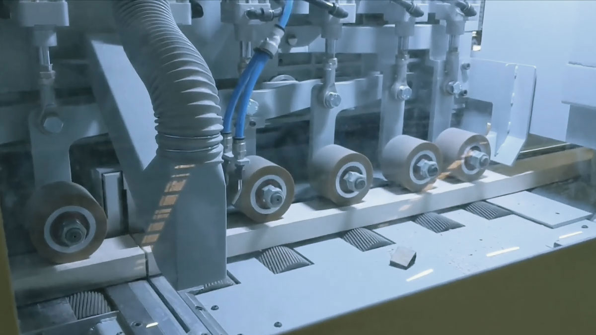 A conveyor system with multiple wooden planks being transported in a woodworking facility, featuring an industrial rip saw for processing the wood.