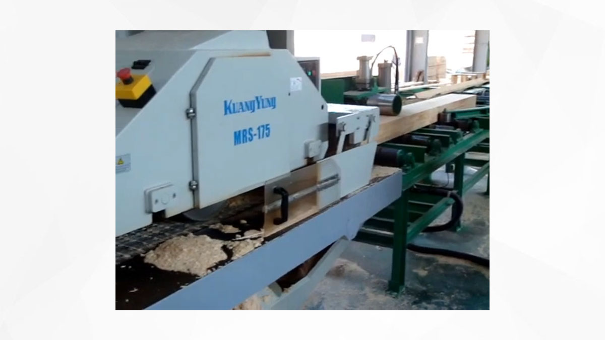 A conveyor system with multiple wooden planks being transported in a woodworking facility, featuring an industrial rip saw for processing the wood.